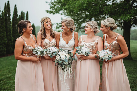 Bridal party in rose gold dresses laughing and holding bouquets of flowers