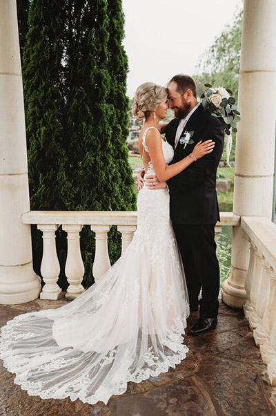 Bride and groom posing together on porch with ivory pillars