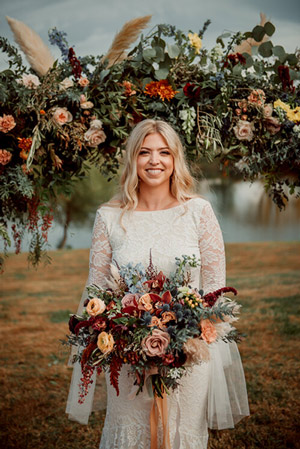 Bride posing with bouquet and arch full of flowers