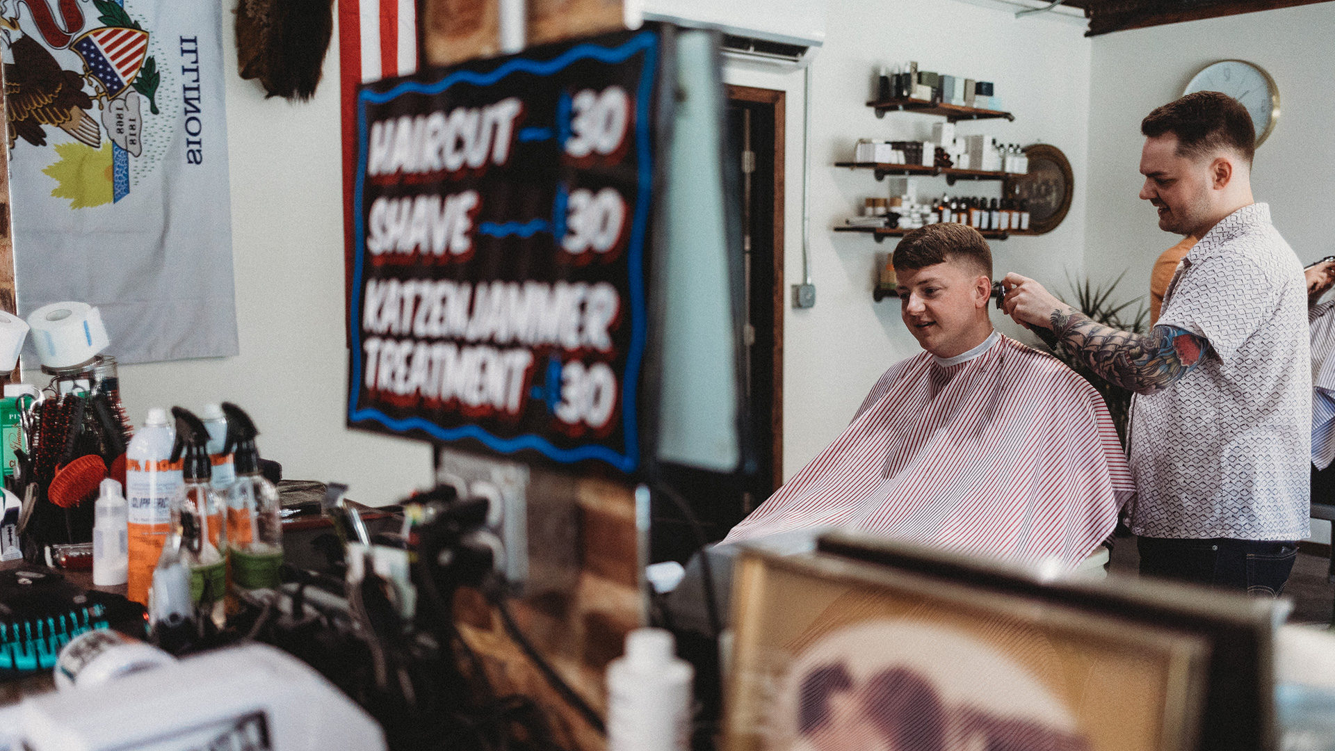 Barber cutting hair with pricing sign and cutting supplies in background